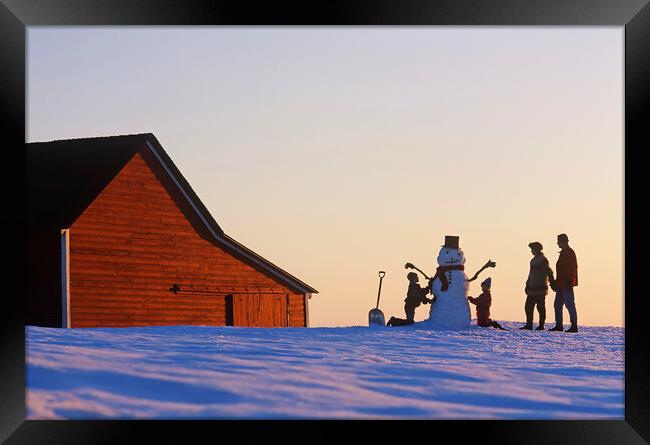 a family make a snowman in front of a red barn Framed Print by Dave Reede