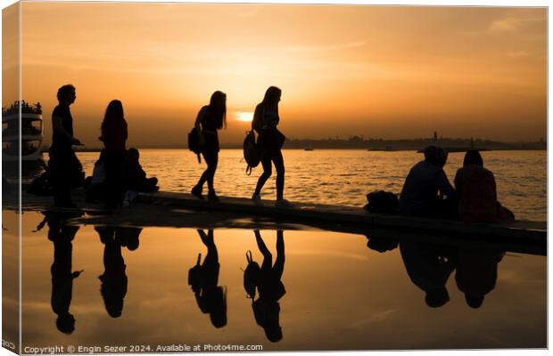Silhouettes of some young people with beautiful reflections on the water at sunset Canvas Print by Engin Sezer