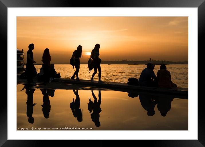 Silhouettes of some young people with beautiful reflections on the water at sunset Framed Mounted Print by Engin Sezer