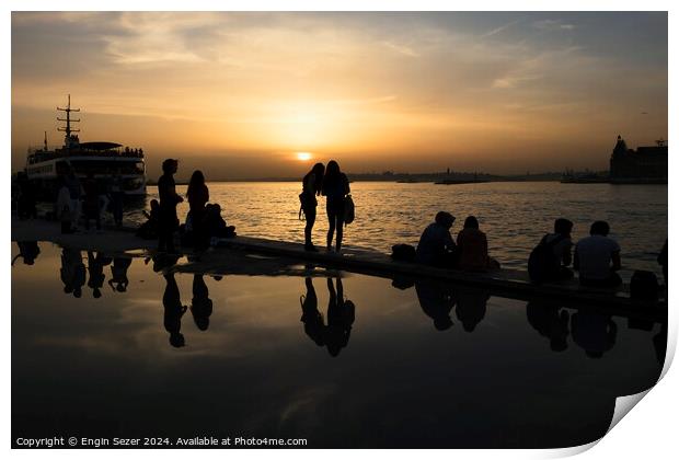 Silhouettes of some young people with beautiful reflections on the water at sunset Print by Engin Sezer