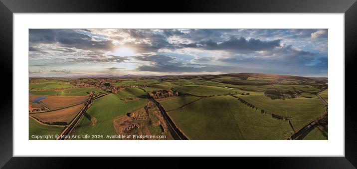 Panoramic aerial view of a scenic landscape with rolling hills, fields, and a winding road under a dramatic sky at sunset. Framed Mounted Print by Man And Life