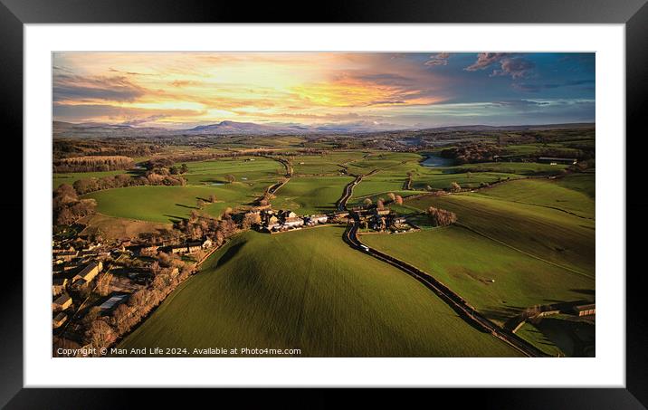Aerial view of a scenic countryside at sunset with lush green fields, a small village, and a winding road leading towards distant hills. Framed Mounted Print by Man And Life