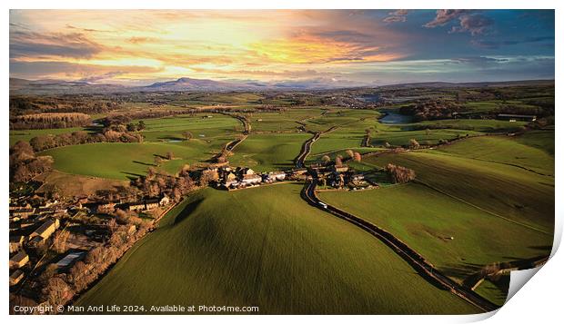 Aerial view of a scenic countryside at sunset with lush green fields, a small village, and a winding road leading towards distant hills. Print by Man And Life