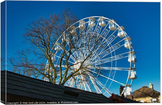 Ferris wheel against a clear blue sky, partially obscured by a rooftop, with bare trees in the background in Lancaster. Canvas Print by Man And Life