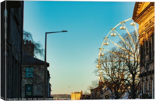 Urban sunset scene with silhouette of a Ferris wheel against a clear sky, flanked by historic buildings and a street lamp in Lancaster. Canvas Print by Man And Life