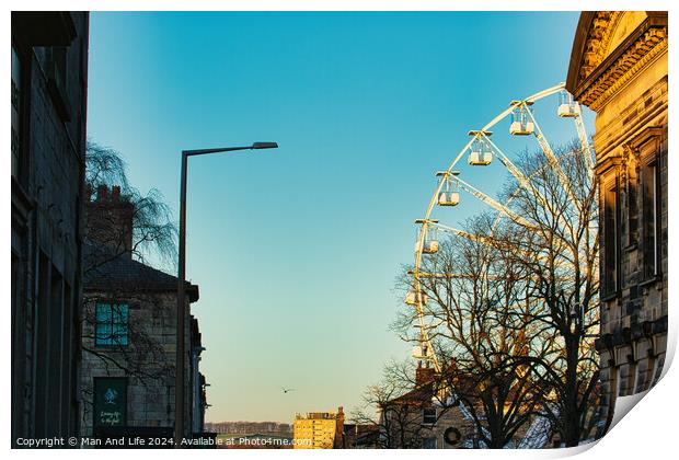 Urban sunset scene with silhouette of a Ferris wheel against a clear sky, flanked by historic buildings and a street lamp in Lancaster. Print by Man And Life