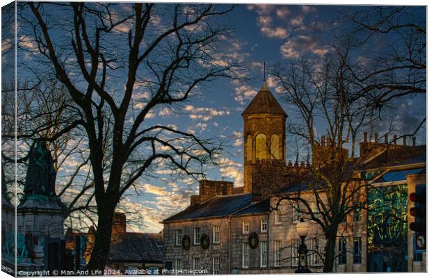 Historic stone building with a clock tower at dusk, silhouetted trees, and a vibrant sky in Lancaster. Canvas Print by Man And Life
