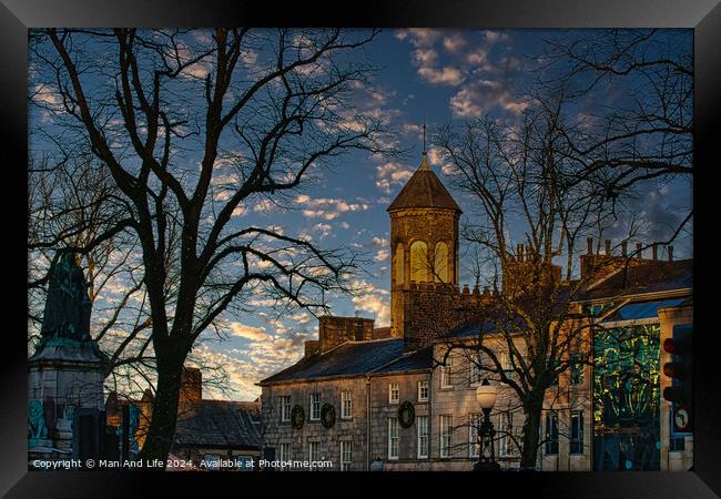 Historic stone building with a clock tower at dusk, silhouetted trees, and a vibrant sky in Lancaster. Framed Print by Man And Life