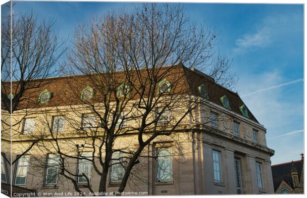 Classic European building facade with bare tree branches against a clear blue sky at dusk. Canvas Print by Man And Life