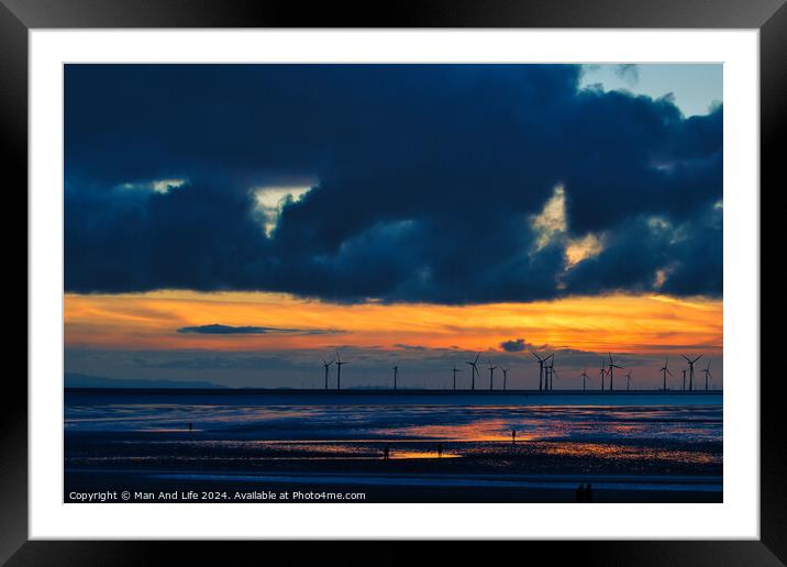 Dramatic sunset over a beach with silhouetted wind turbines on the horizon and reflective wet sand in Crosby, England. Framed Mounted Print by Man And Life