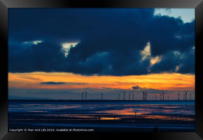 Dramatic sunset over a beach with silhouetted wind turbines on the horizon and reflective wet sand in Crosby, England. Framed Print by Man And Life