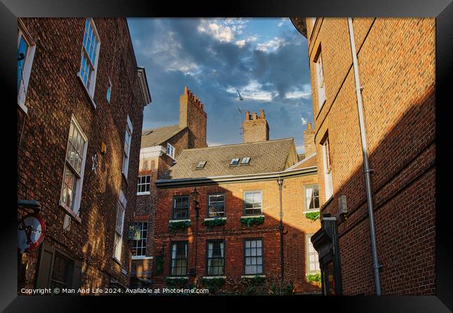 Charming European alleyway with historic brick buildings and a glimpse of blue sky with clouds in York, UK. Framed Print by Man And Life