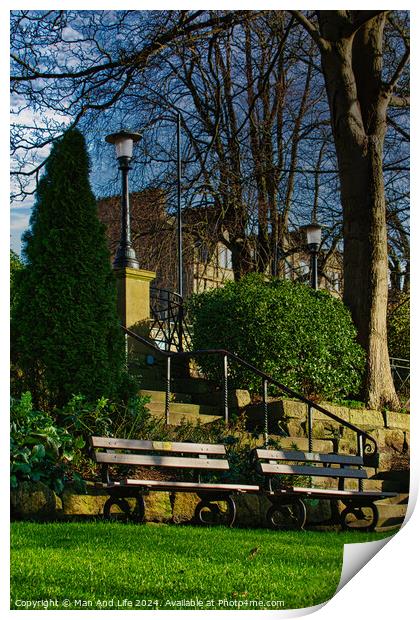 Tranquil park scene with empty benches, lush greenery, and a street lamp against a clear blue sky in Harrogate, England. Print by Man And Life