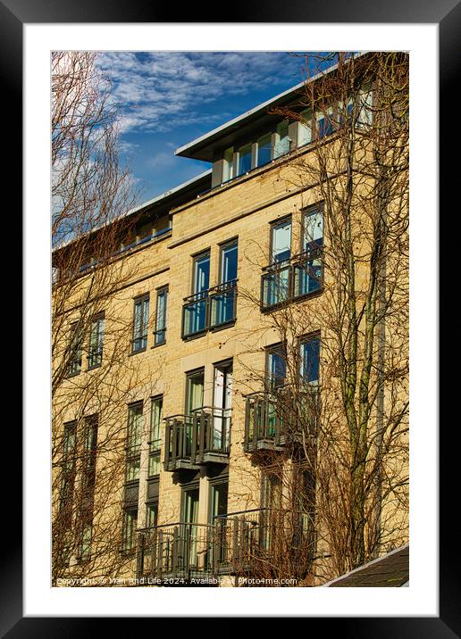 Facade of a modern apartment building with balconies, framed by leafless trees against a clear blue sky in Harrogate, England. Framed Mounted Print by Man And Life