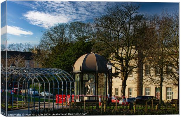Urban park scene with modern glass pavilion, traditional street lamp, and lush trees under a blue sky with wispy clouds in Harrogate, England. Canvas Print by Man And Life