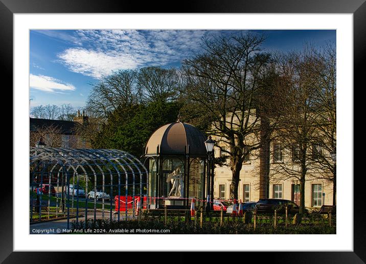 Urban park scene with modern glass pavilion, traditional street lamp, and lush trees under a blue sky with wispy clouds in Harrogate, England. Framed Mounted Print by Man And Life