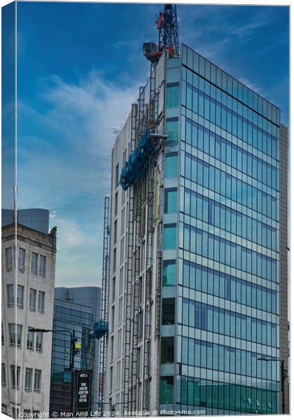 Modern glass building facade with reflections under a cloudy sky, surrounded by urban architecture in Leeds, UK. Canvas Print by Man And Life