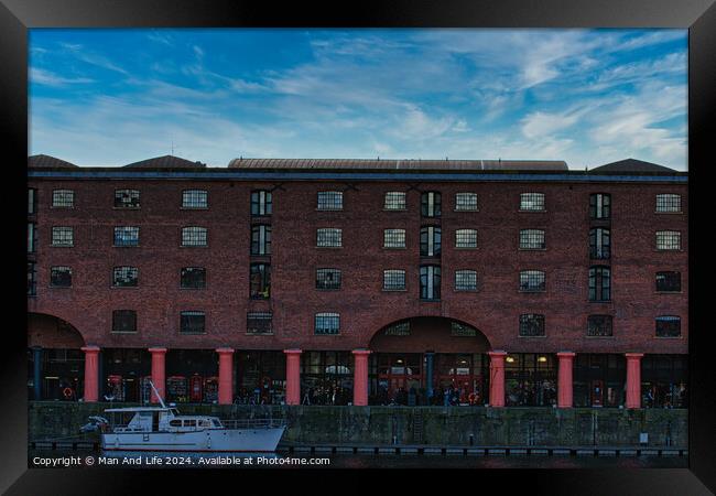 Brick warehouse with arched supports by a canal with a moored boat under a clear blue sky in Liverpool, UK. Framed Print by Man And Life
