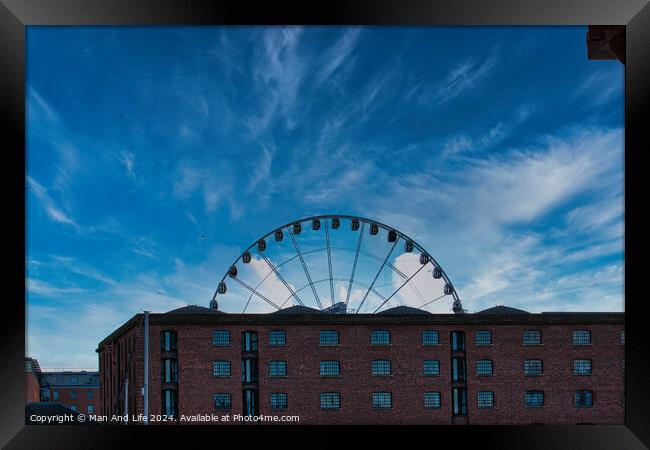 Ferris wheel silhouette against a blue sky with wispy clouds, framed by buildings in Liverpool, UK. Framed Print by Man And Life