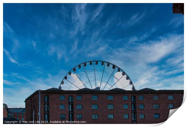 Ferris wheel silhouette against a blue sky with wispy clouds, framed by buildings in Liverpool, UK. Print by Man And Life