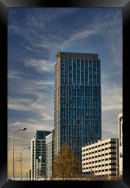 Modern glass skyscraper against a blue sky with clouds, surrounded by urban architecture in Liverpool, UK. Framed Print by Man And Life