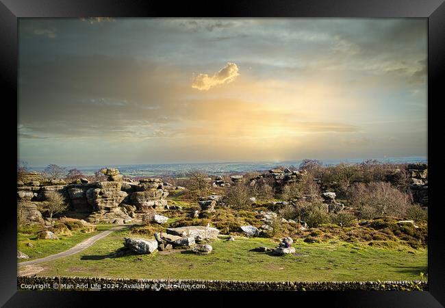 Picturesque rural landscape at sunset with rocky formations and green fields under a cloudy sky at Brimham Rocks, in North Yorkshire Framed Print by Man And Life