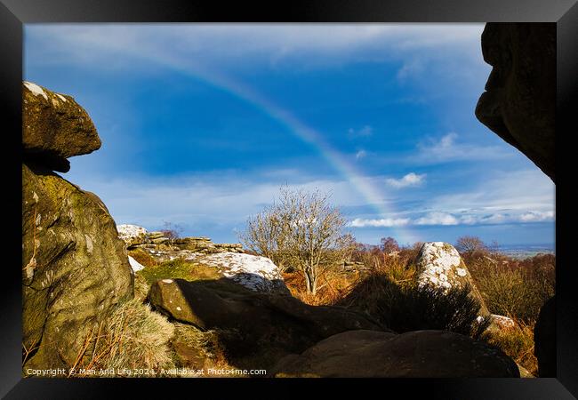 Scenic landscape with a rainbow over a solitary tree, framed by rocky outcrops under a blue sky with clouds at Brimham Rocks, in North Yorkshire Framed Print by Man And Life