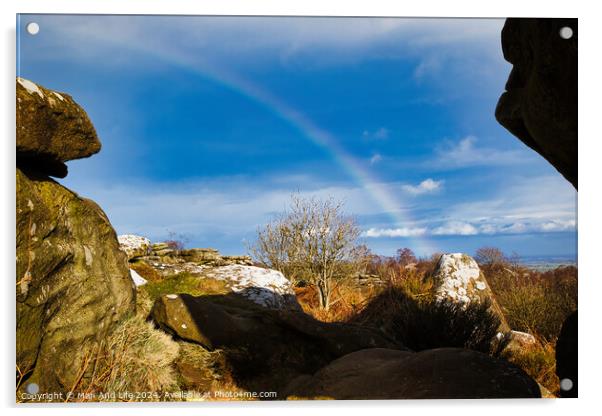 Scenic landscape with a rainbow over a solitary tree, framed by rocky outcrops under a blue sky with clouds at Brimham Rocks, in North Yorkshire Acrylic by Man And Life