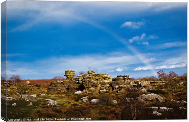 Vibrant rainbow over a rocky landscape with scattered boulders and lush greenery under a blue sky with clouds at Brimham Rocks, in North Yorkshire Canvas Print by Man And Life
