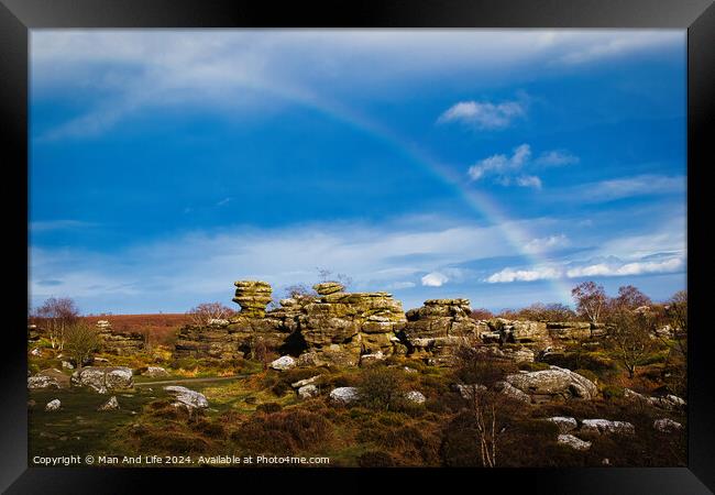 Vibrant rainbow over a rocky landscape with scattered boulders and lush greenery under a blue sky with clouds at Brimham Rocks, in North Yorkshire Framed Print by Man And Life