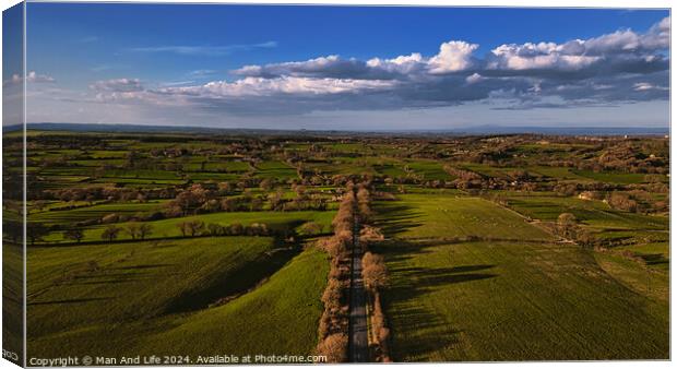 Aerial view of a lush green countryside with a road cutting through, under a vast blue sky with scattered clouds in North Yorkshire. Canvas Print by Man And Life