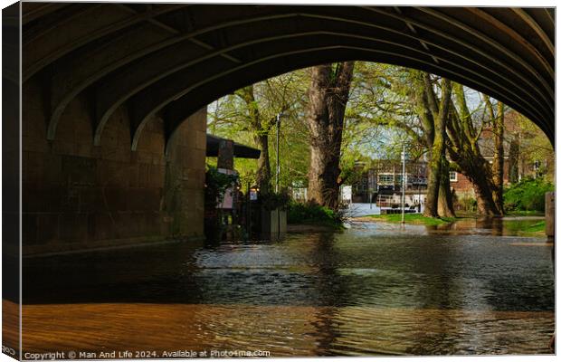 Tranquil river flowing under an arched stone bridge with lush green trees and a hint of urban life in the background, showcasing a blend of nature and city architecture in York, North Yorkshire, England. Canvas Print by Man And Life
