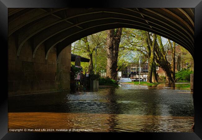 Tranquil river flowing under an arched stone bridge with lush green trees and a hint of urban life in the background, showcasing a blend of nature and city architecture in York, North Yorkshire, England. Framed Print by Man And Life