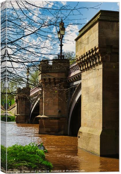 Scenic view of an old stone bridge with arches over a river, framed by blue skies and greenery, with a vintage street lamp adding to the historic charm in York, North Yorkshire, England. Canvas Print by Man And Life