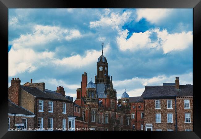 Dramatic clouds loom over a historic town center, featuring a prominent clock tower and classic brick buildings, capturing a quintessential British townscape in York, North Yorkshire, England. Framed Print by Man And Life
