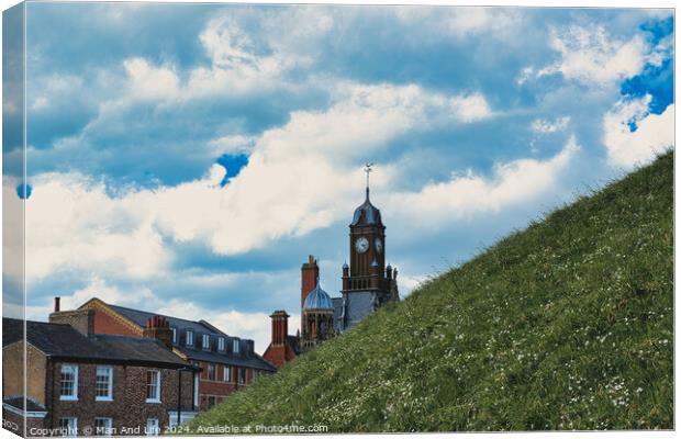 Quaint European town with historic buildings and a clock tower, set against a vibrant blue sky with fluffy clouds, and a lush green hill in the foreground in York, North Yorkshire, England. Canvas Print by Man And Life