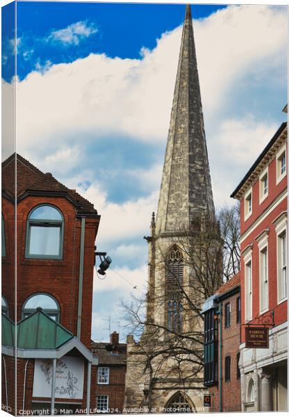 Vertical shot of an ancient church spire reaching into a blue sky with clouds, flanked by traditional brick buildings, showcasing architectural contrast and historical cityscape in York, North Yorkshire, England. Canvas Print by Man And Life