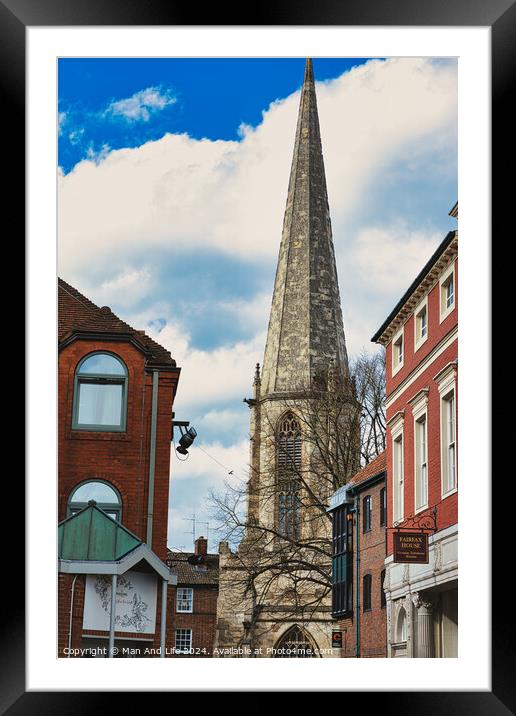 Vertical shot of an ancient church spire reaching into a blue sky with clouds, flanked by traditional brick buildings, showcasing architectural contrast and historical cityscape in York, North Yorkshire, England. Framed Mounted Print by Man And Life