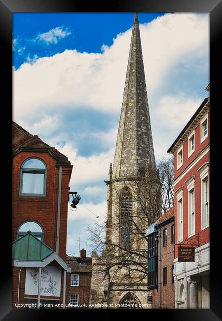 Vertical shot of an ancient church spire reaching into a blue sky with clouds, flanked by traditional brick buildings, showcasing architectural contrast and historical cityscape in York, North Yorkshire, England. Framed Print by Man And Life