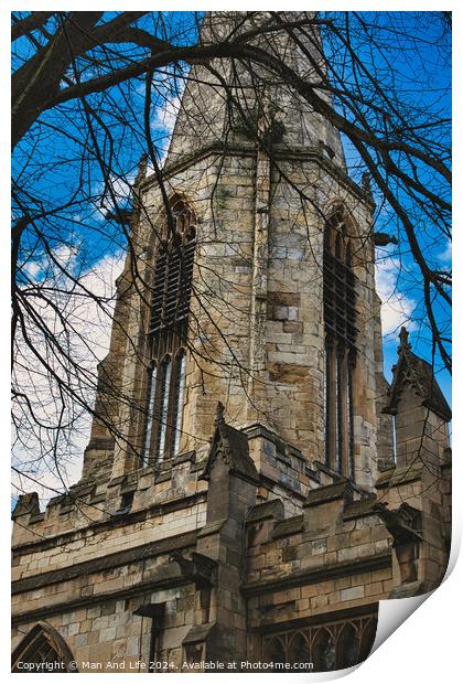 Gothic church tower with intricate stone details, framed by bare tree branches against a blue sky with fluffy clouds in York, North Yorkshire, England. Print by Man And Life