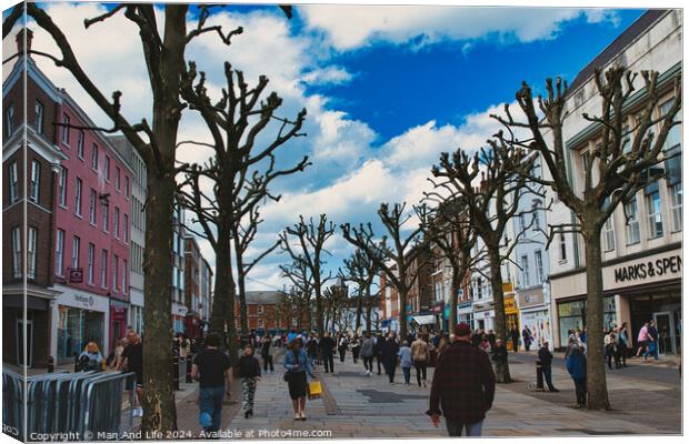 Vibrant city street bustling with pedestrians, lined with leafless pruned trees against a dynamic blue sky with fluffy clouds, showcasing urban life and seasonal change in York, North Yorkshire, England. Canvas Print by Man And Life