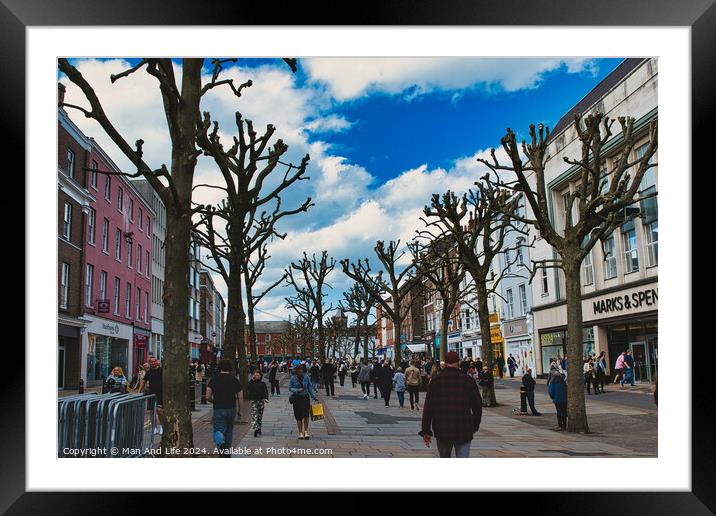 Vibrant city street bustling with pedestrians, lined with leafless pruned trees against a dynamic blue sky with fluffy clouds, showcasing urban life and seasonal change in York, North Yorkshire, England. Framed Mounted Print by Man And Life