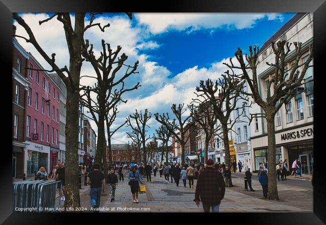 Vibrant city street bustling with pedestrians, lined with leafless pruned trees against a dynamic blue sky with fluffy clouds, showcasing urban life and seasonal change in York, North Yorkshire, England. Framed Print by Man And Life