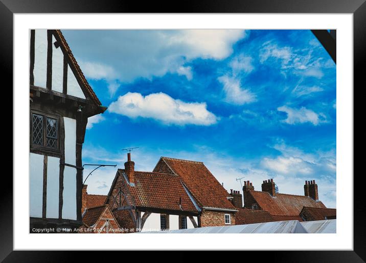 Quaint European village with traditional half-timbered houses and terracotta rooftops under a vibrant blue sky with fluffy clouds in York, North Yorkshire, England. Framed Mounted Print by Man And Life