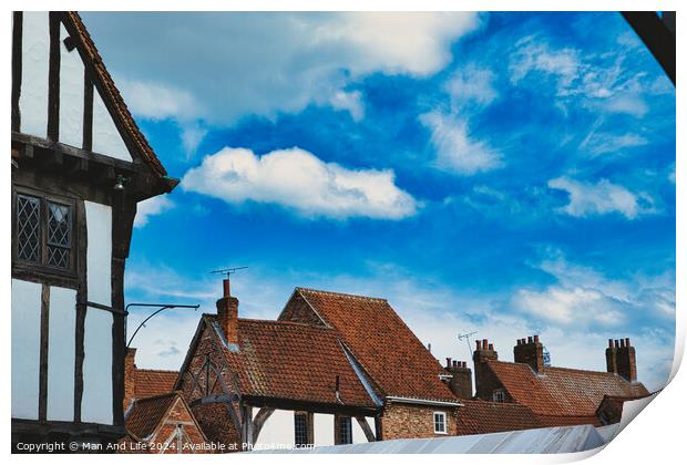 Quaint European village with traditional half-timbered houses and terracotta rooftops under a vibrant blue sky with fluffy clouds in York, North Yorkshire, England. Print by Man And Life