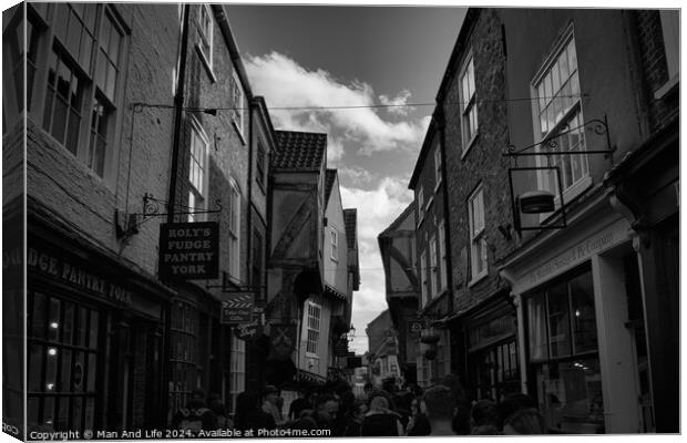 Black and white image of a bustling narrow street in York, with historic buildings, quaint shops, and pedestrians exploring the charming old town in York, North Yorkshire, England. Canvas Print by Man And Life