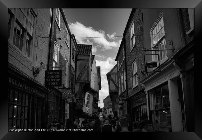 Black and white image of a bustling narrow street in York, with historic buildings, quaint shops, and pedestrians exploring the charming old town in York, North Yorkshire, England. Framed Print by Man And Life