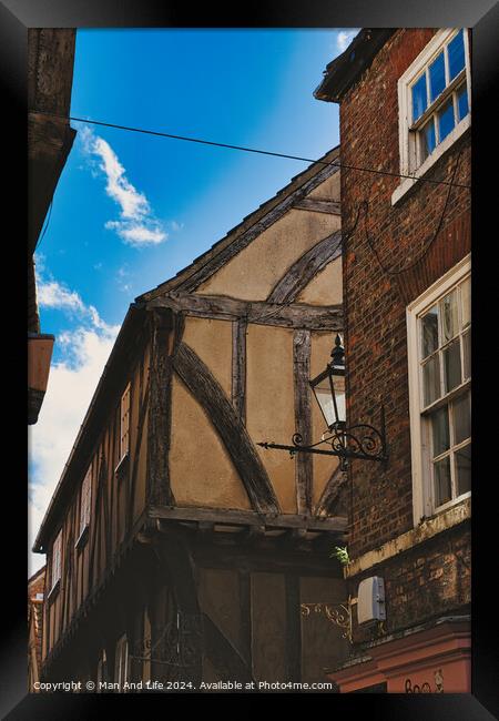 Quaint half-timbered building with exposed wooden beams under a clear blue sky, showcasing traditional architectural details and a vintage street lamp in York, North Yorkshire, England. Framed Print by Man And Life