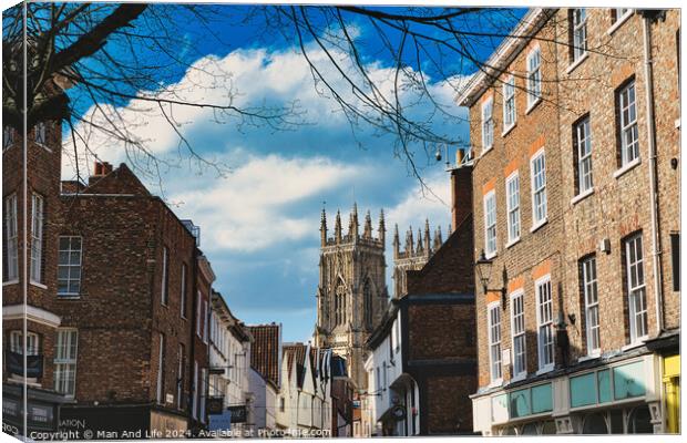 Historic European city street with traditional brick buildings and a prominent Gothic cathedral in the background under a blue sky with clouds in York, North Yorkshire, England. Canvas Print by Man And Life