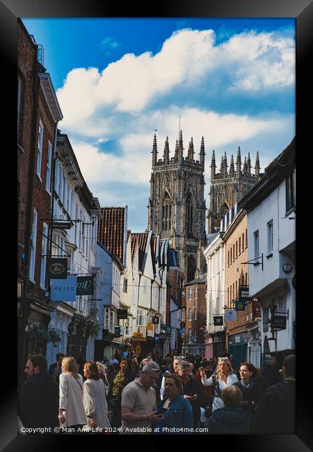 Bustling street scene with pedestrians in a historic city center, featuring old buildings and a prominent Gothic cathedral under a cloudy sky in York, North Yorkshire, England. Framed Print by Man And Life